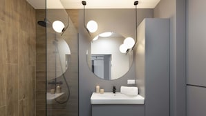 A modern bathroom with a glass-enclosed shower, a round mirror with lights, a white sink, and a grey cabinet. - Elite Apartments Seastory (Gdansk)