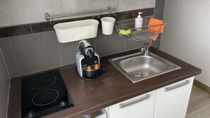 Una cocina con estufa, lavaplatos y un escurreplatos con utensilios.
