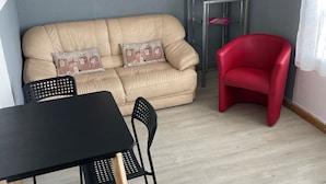 Una sala de estar con un sofá color beige, un sillón rojo, una mesa negra y una mesita auxiliar con un marco de foto.