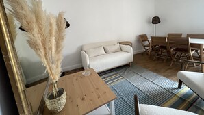 A living room with a sofa, wooden dining table, chairs, a mirror, and a vase with pampas grass. - Appartement T3 vue mer (Toulon)