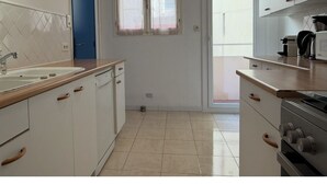 A kitchen with white cabinets, a blue door, and a window. - Appartement T3 vue mer (Toulon)