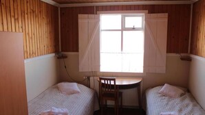 Een kleine kamer met twee eenpersoonsbedden, een houten bureau en een raam met luiken.
