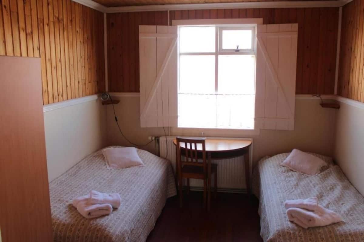 Una habitación pequeña con dos camas individuales, un escritorio de madera y una ventana con contraventanas.