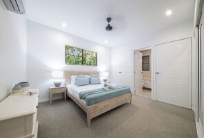 A bedroom with a bed, bedside tables, a window with blinds, a ceiling fan, and a wardrobe.