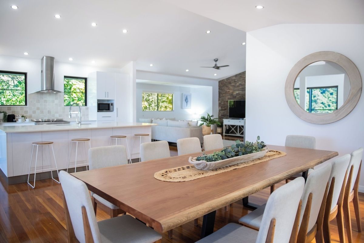 A modern kitchen with white cabinetry, a wooden dining table, and bar stools.