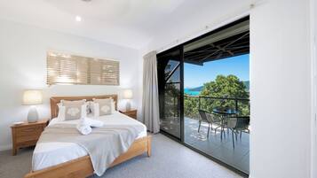 A bedroom with a large bed, bedside tables, a window with blinds, and a balcony with outdoor furniture.