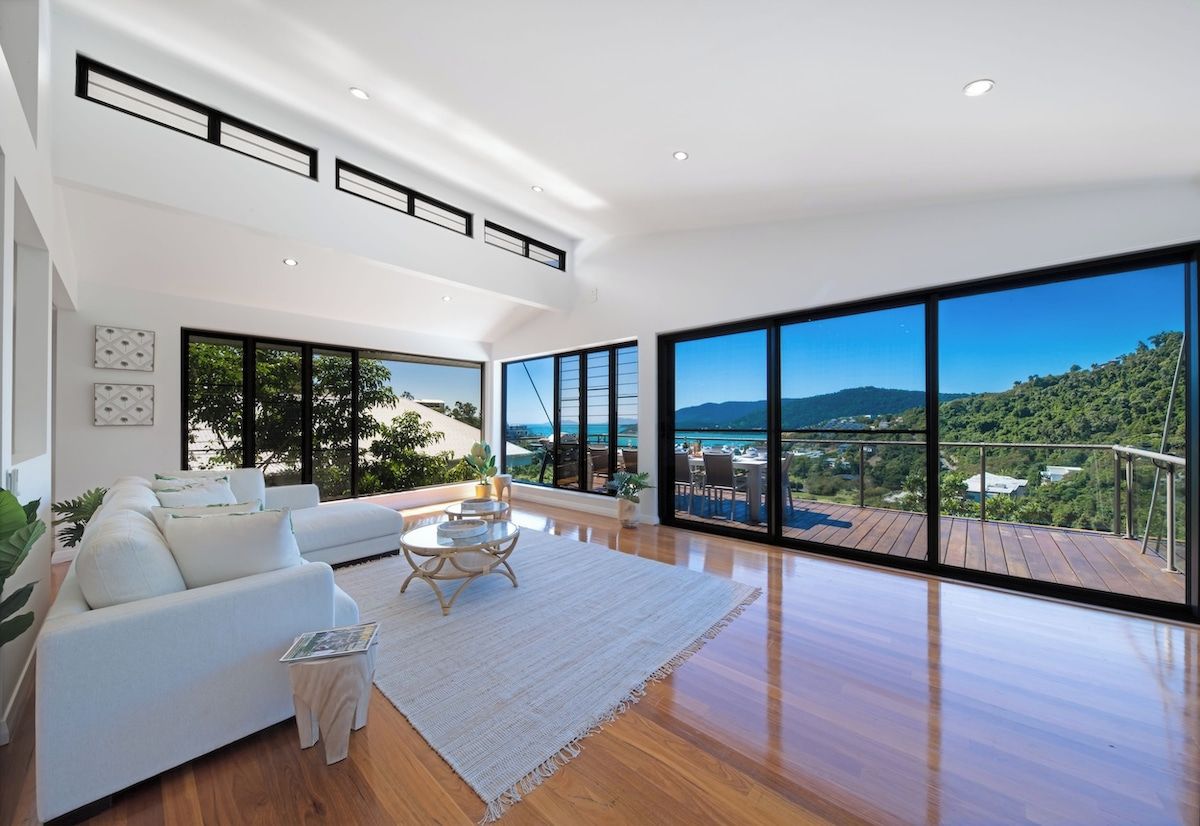 A spacious living room with a large window, a white sofa, a coffee table, and a view of a deck and landscape.