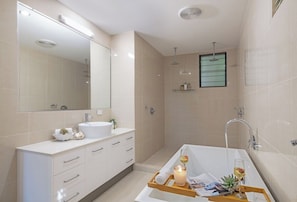 A modern bathroom with a bathtub, a large mirror, and a shower area.
