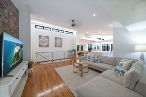 Una sala de estar moderna con un televisor de pantalla plana grande, un sofá, una mesa de centro y una escalera que lleva a un nivel superior.