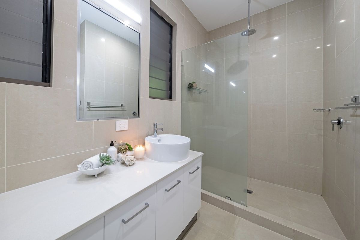 Un baño moderno con un tocador blanco, un lavabo redondo, cabina de ducha con mampara de cristal y un espejo sobre el tocador.
