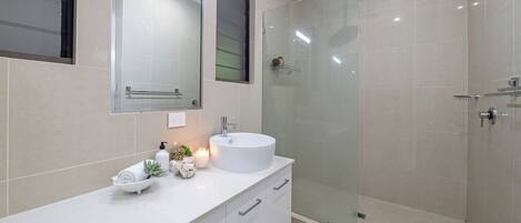 Un baño moderno con un tocador blanco, un lavabo redondo, cabina de ducha con mampara de cristal y un espejo sobre el tocador.