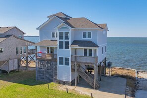 A two-story beach house with a balcony and a deck, overlooking the ocean.