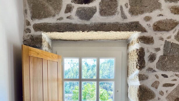 Une pièce aux murs de pierre, avec une porte blanche, un meuble en bois et une vue sur la verdure à l’extérieur.