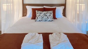 Un lit bien fait, avec des draps blancs, deux oreillers et un coussin décoratif orné d’un motif de feuilles.