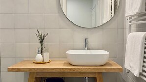 Une salle de bain moderne avec un meuble-lavabo en bois, un miroir rond, un lavabo blanc et un porte-serviettes.