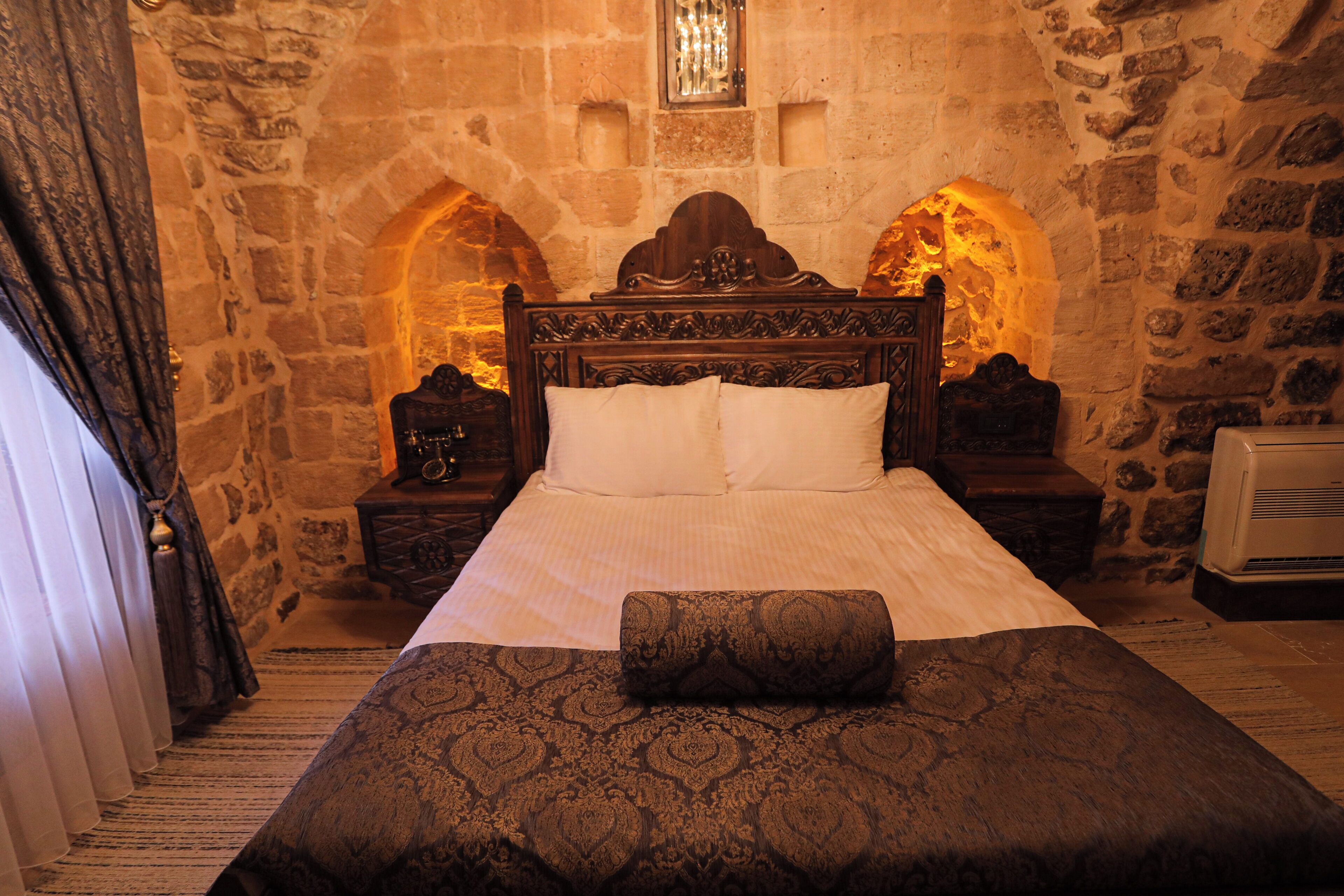 A traditional stone-walled bedroom with a large bed, two nightstands, and a stone fireplace.