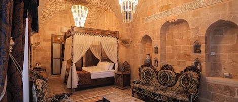 A historic room with a four-poster bed, ornate furniture, and stone walls.