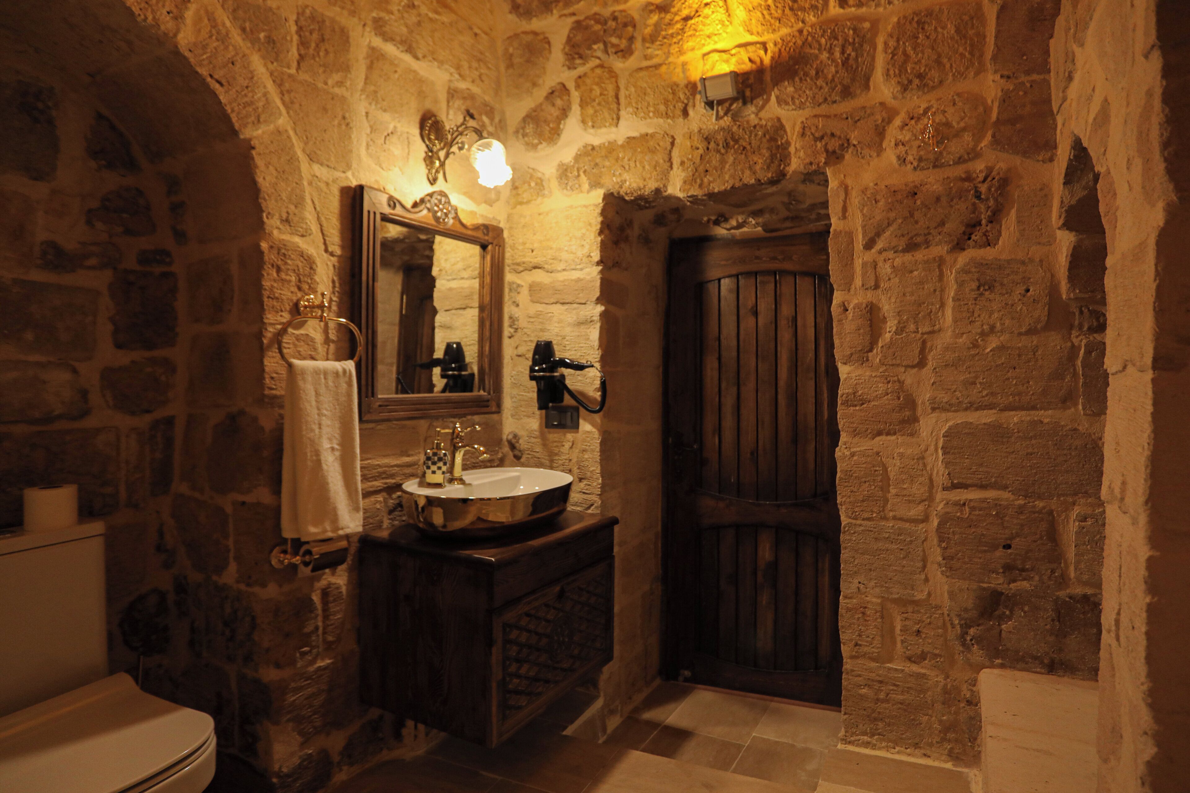 A stone-walled bathroom with a wooden door, a sink with a mirror, and a towel rack.