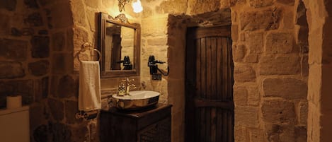 A stone-walled bathroom with a wooden door, a sink with a mirror, and a towel rack.