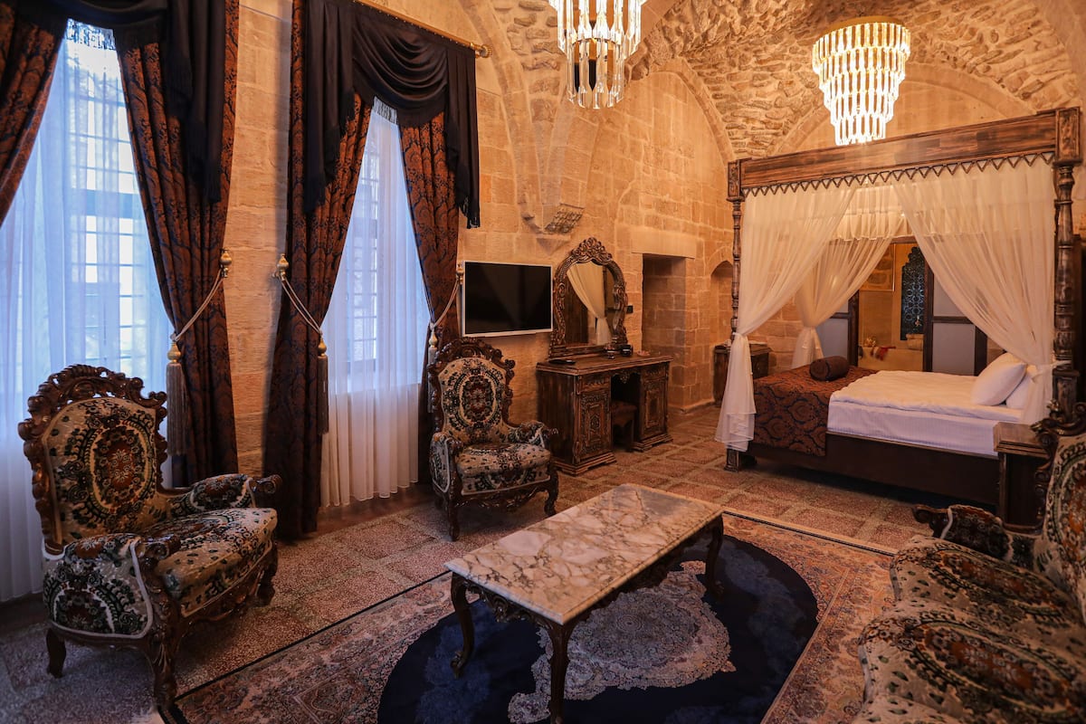 A room with a four-poster bed, ornate chairs, a marble table, and a chandelier.