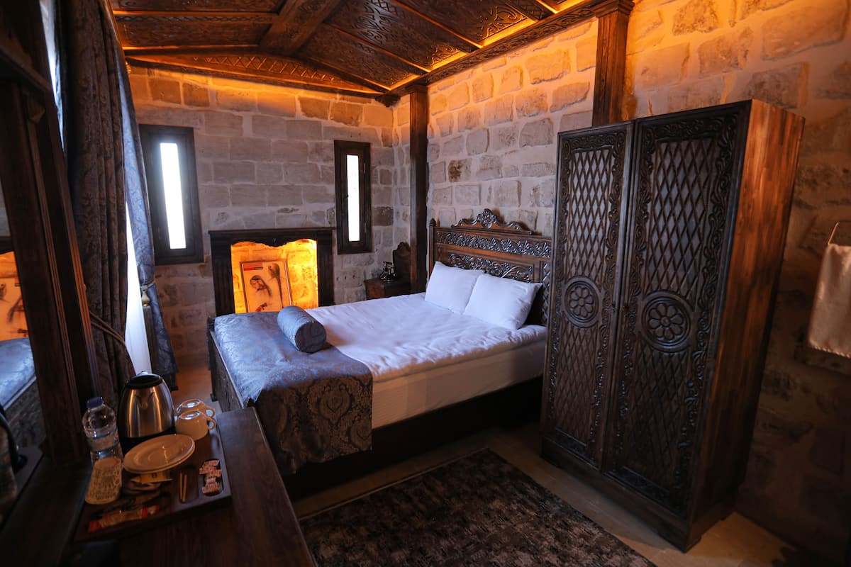 A traditional room with a stone wall, a wooden bed, a wardrobe, and a small table with a kettle and cups.