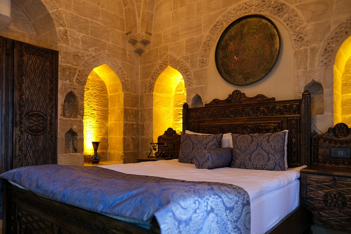 A room with a large bed, stone walls, and a wooden headboard.