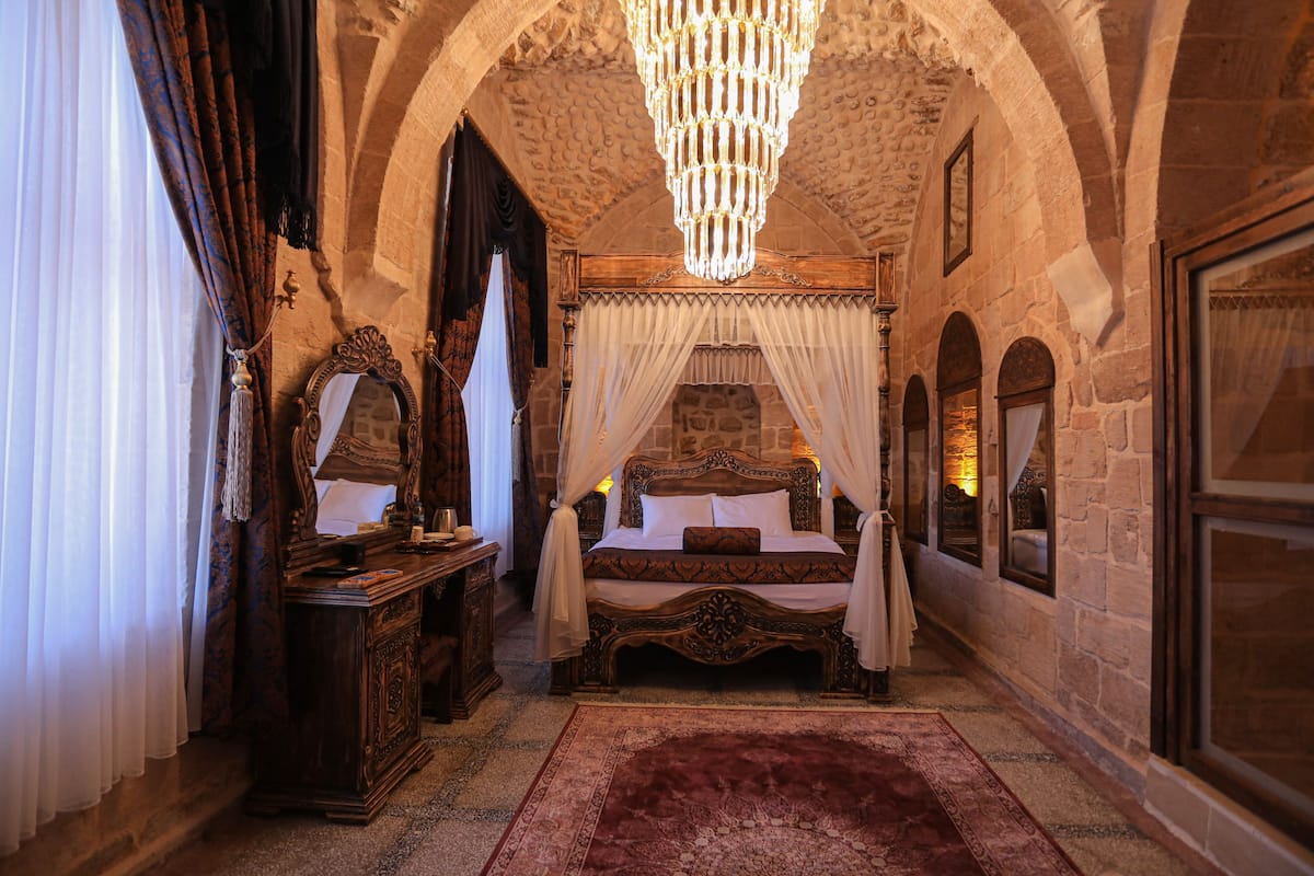 A bedroom with a four-poster bed, a chandelier, and stone walls.
