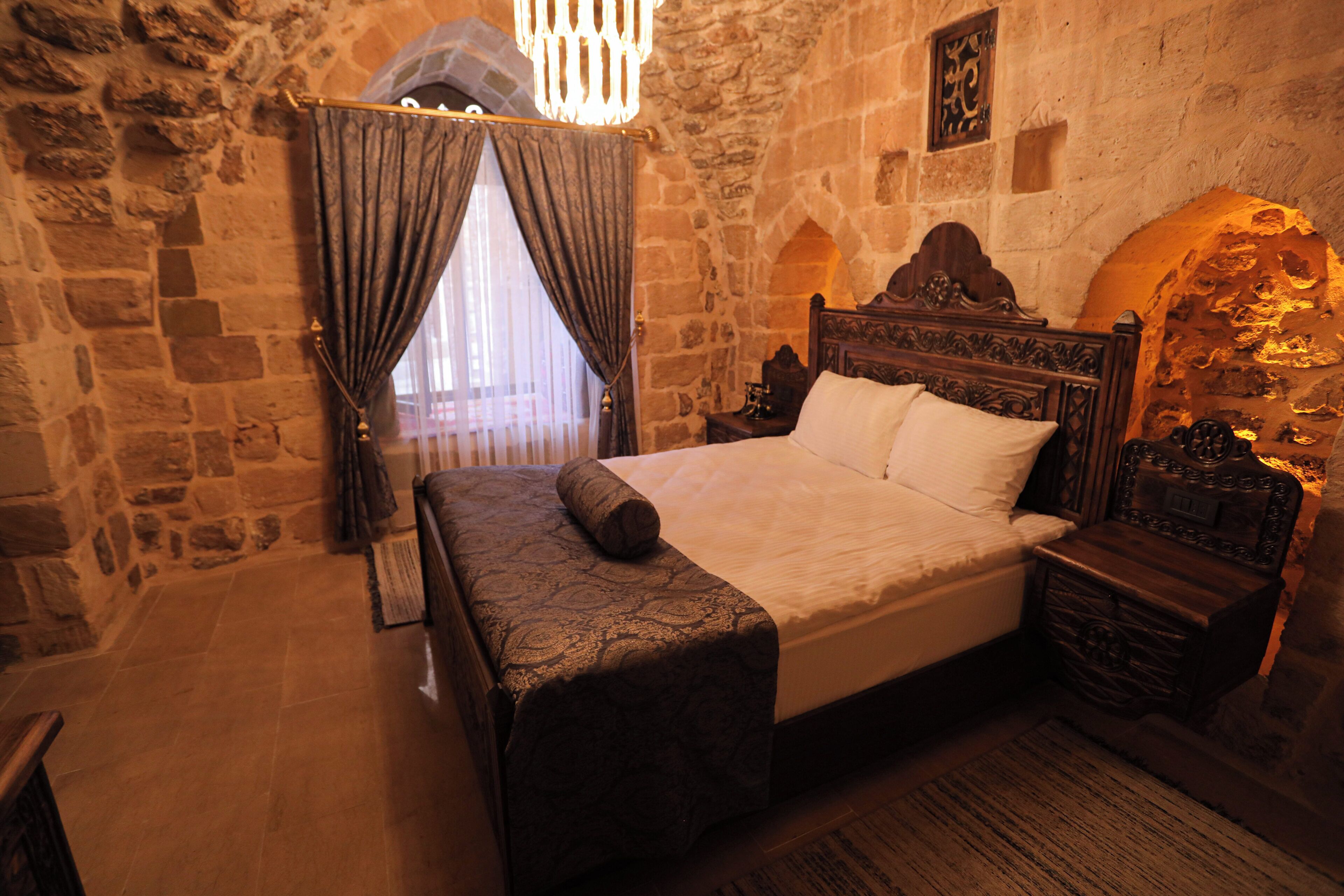 A bedroom with a stone wall, a wooden bed, a nightstand, and a chandelier.