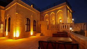 Un área de comedor al aire libre con paredes de piedra y ventanas arqueadas, iluminada con cálida luz.