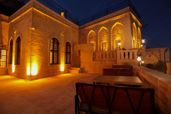An outdoor dining area with stone walls and arched windows, illuminated by warm lighting.