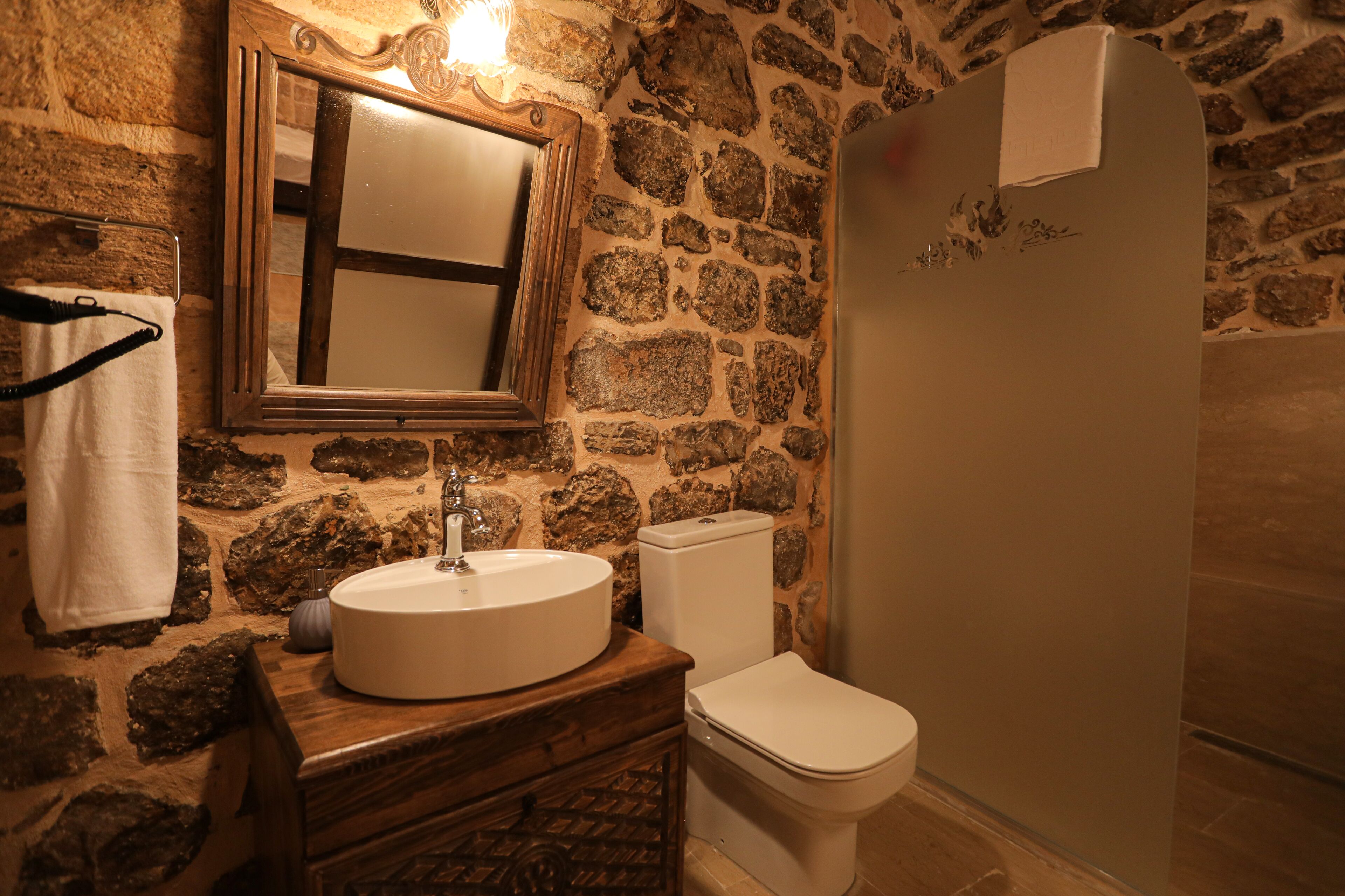 Une salle de bain avec un mur en pierre, un meuble-lavabo en bois, un évier, des toilettes et un miroir.