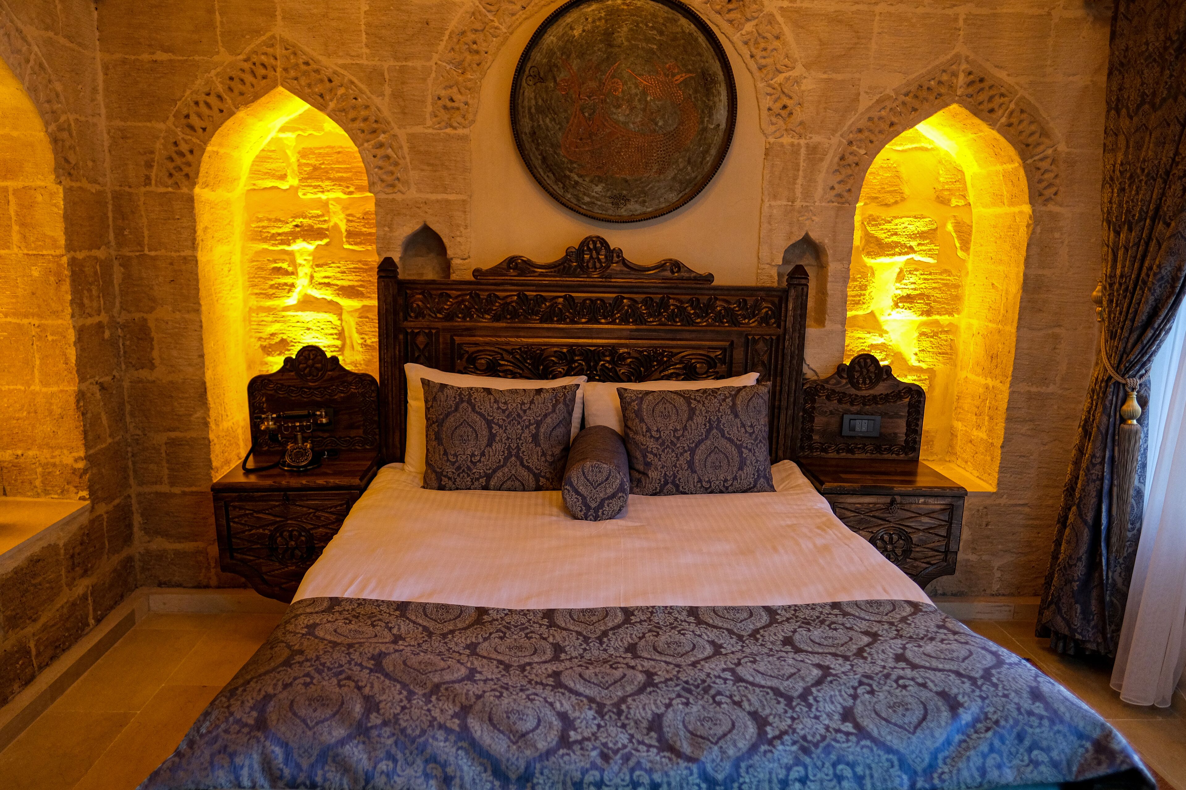 Un letto con copriletto decorato, una testiera in legno e due comodini con oggetti ornamentali.