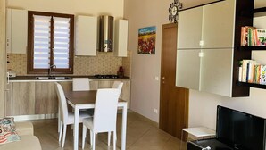 Une cuisine moderne avec des meubles en bois, un coin repas avec des chaises blanches, un canapé et un meuble pour la télévision.
