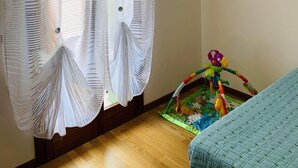 Une pièce avec un plancher en bois, un lit recouvert d’une couverture bleue, un tapis de jeu coloré et un rideau à motifs rayés.