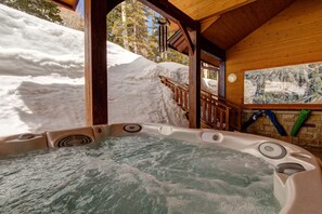 Un jacuzzi en una cabaña de madera con exterior nevado y vista a árboles.