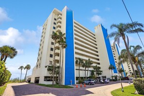 A multi-story hotel with a prominent blue vertical stripe, palm trees, and a paved driveway.