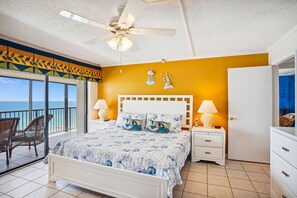 A bedroom with a bed, nightstands, a ceiling fan, and a view of the ocean.