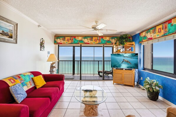 A living room with a red sofa, a glass coffee table, and a view of the ocean through large windows.