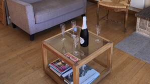Een moderne woonkamer met een grijze bank, een houten salontafel met tijdschriften, een houten stoel en een aan de muur bevestigde televisie.