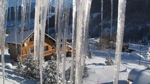 Een houten chalet met balkon, omgeven door sneeuwbedekte bomen en bergen.