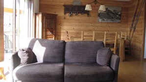 Een houten interieur met een bank, houten wanden, een schilderij en een ski-rek.