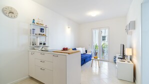Et moderne køkken med hvide skabe, en central ø og et spiseområde med en blå sofa og et lille bord.