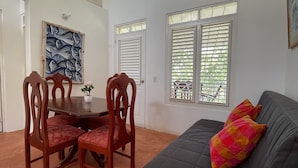 A room with a dark-colored sofa, a dining table with chairs, and a window with blinds. - Casa yann  (Las Galeras)