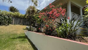 A house with a white exterior, a covered porch, and a well-maintained garden with various plants and flowers. - Casa yann  (Las Galeras)