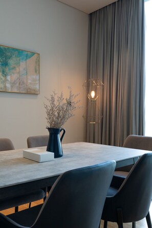 Uma sala de jantar moderna com mesa, cadeiras, um vaso com flores secas, uma luminária geométrica e um quadro na parede.