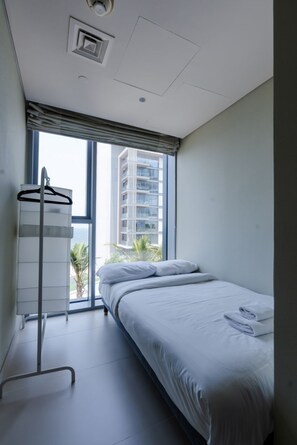 A hotel room with a bed, a window with a view of a building, and a towel rack. - Nasma Luxury Stays - Bluewaters Residences Building 4 (Dubai)