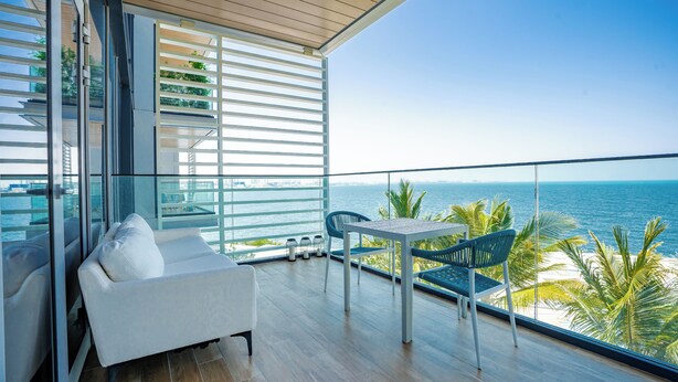 A balcony with a white sofa, a table, and chairs, overlooking a clear view of the ocean.