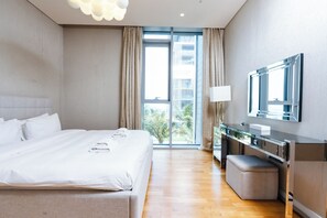 A modern hotel room with a large bed, a vanity with a mirror, and a view of palm trees through the window.