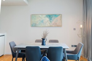 A modern dining area with a rectangular table, six chairs, a vase with dried flowers, a painting on the wall, and a floor lamp. - Nasma Luxury Stays - Bluewaters Residences Building 4 (Dubai)