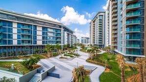 A modern residential complex with multiple high-rise buildings, a central pedestrian pathway, and landscaped areas with palm trees.